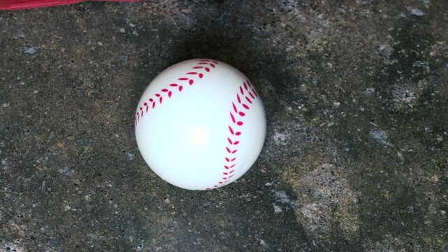 White baseball with red stitching on dark concrete ground top view sports equipment background