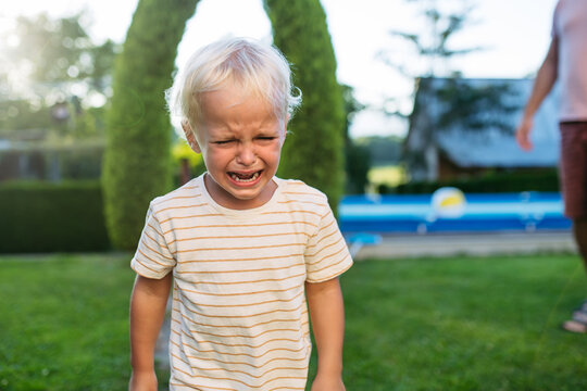 Crying toddler boy standing in garden with strong emotion.