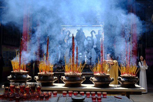 Woman prays among smoking incense urns inside Ba Thien Hau Temple.  Ho Chi Minh city. Vietnam.