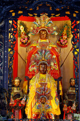 Fototapeta premium Ba Thien Hau Temple. Ornate wooden shrine with lacquered carvings frames three golden Taoist deity statues. Ho Chi Minh city. Vietnam.