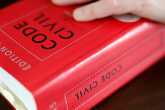 A hand rests solemnly on the red cover of a French Code Civil legal reference book.