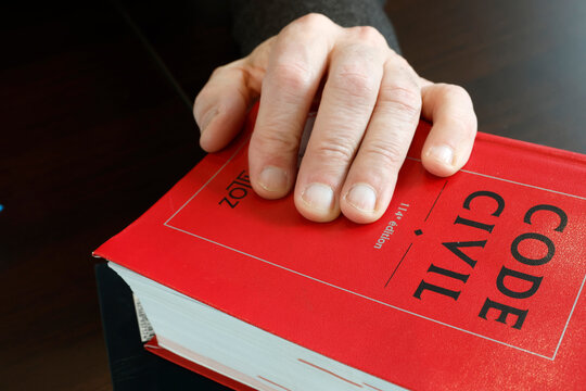 A hand rests solemnly on the red cover of a French Code Civil legal reference book.