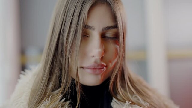 Young beautiful woman confidence look in studio during photo session. Young woman model with long loose hair confidently poses in fur coat for camera closeup. Model posing urban avenue.