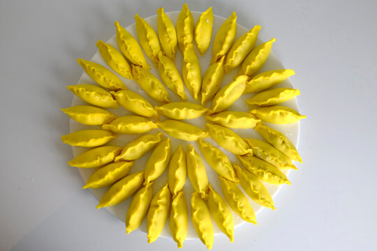 Vibrant yellow saffron dumplings arranged in a circular sunflower pattern on white plate.