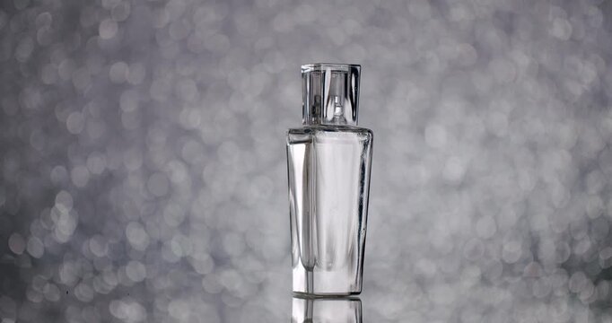 A sleek glass perfume bottle stands on a reflective surface with a sparkling bokeh background, exuding elegance and luxury. Elegant Glass Perfume Bottle On Shiny Reflective Surface