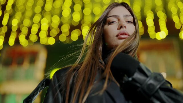 Beautiful woman posing for the camera against the background of the lights. Portrait of a young woman against the background of night lights. Pretty female person posing in city center at night.