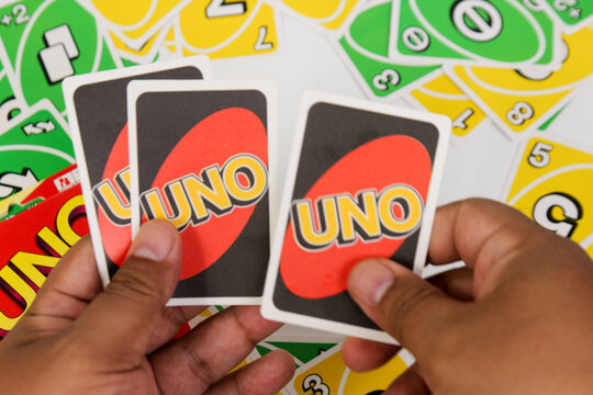 Uno Card Game Being Played by Hands Holding Red and Black Cards with Colorful Yellow and Green Number Cards Scattered on a White Background