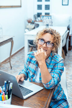 Smiling woman working on laptop in bright home office wearing glasses and a blue plaid shirt