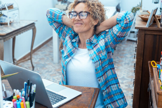 Relaxed woman stretching at her home desk while working on a laptop in a bright home office