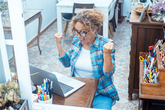 Excited woman celebrating success while working on laptop in a bright home office space