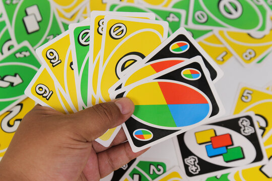Uno Card Game Being Held in a Persons Hand Displaying Yellow Nine Cards Green Skip Cards and Colorful Wild Cards Ready for Strategic Play on a White Background