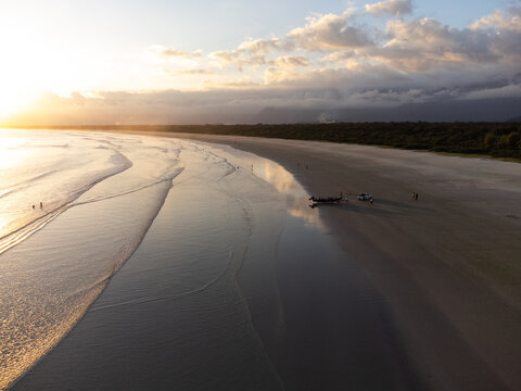 Aerial wide view of Bora Bora beach in Boraceia at sunset with people walking on wet sand mirror in Brazil