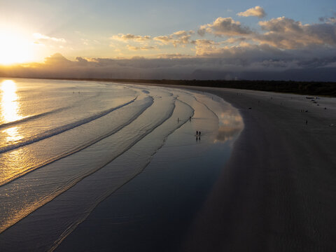 Aerial wide view of Bora Bora beach in Boraceia at sunset with people walking on wet sand mirror in Brazil