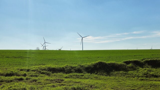 modern wind turbines rise above a vast green field under clear blue sky, capturing renewable energy in peaceful rural landscape