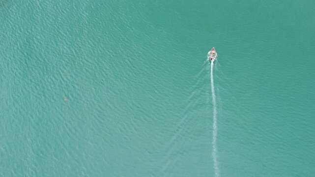 single fishing boat vertically up the screen on turquoise sea with wake