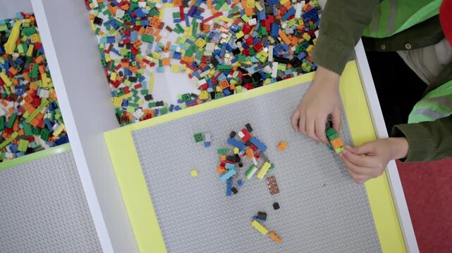 Educational toys for young children. Top view of little boy playing with toy blocks on the table in educational gaming center. Slow motion