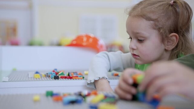 Joyful little cute girl playing with toy blocks on the table in educational gaming center, next to the boy. Slow motion