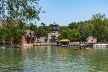 Tourist boats drift across the calm green waters of Kunming Lake at the Summer Palace in Beijing, with traditional pavilions © Extraded