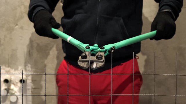 Heavy-duty bolt cutters cutting through a metal wire mesh in an industrial environment. Large scissors for steel. Hands equipment. Handle work is on construction site. High quality 4k footage.