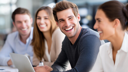 Obraz premium Group of young professionals laughing together during a meeting at a table with a laptop and documents, team bonding and collaboration concept, defocused background, with copy space