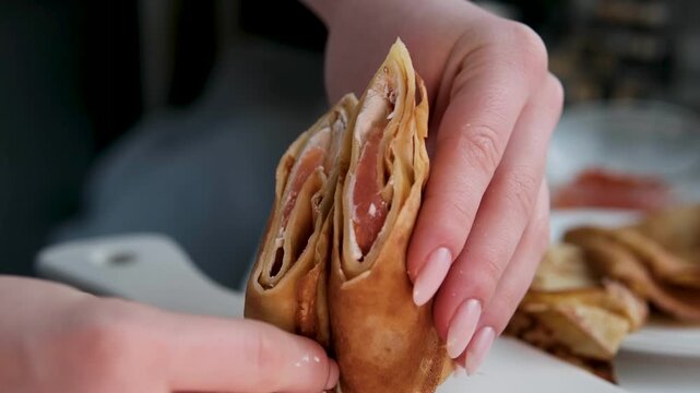 Thin tasty colorful pancakes. Close-up view of red, yellow and green cutaway rolled pancakes with cream cheese and salmon filling on a dish. 4K video. High quality 4k footage