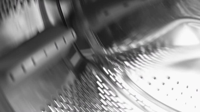 Close-up video of a stainless steel washing machine drum spinning . Circular motion and reflective metal surface create a dynamic pattern, representing household appliance function, cleaning process 