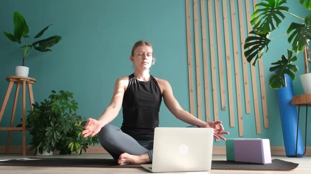 young woman practicing yoga online using laptop and meditating