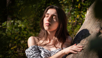 Naklejka premium Peaceful young woman enjoying sunlight by tree trunk