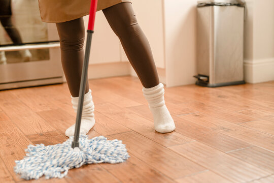 Person mops the floor while wearing socks in a kitchen area during the day