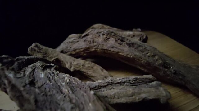 Macro shot of raw Indian Costus roots (Saussurea costus) on a wooden surface. High-quality footage showcasing the natural, dried woody texture of this ancient medicinal herb.