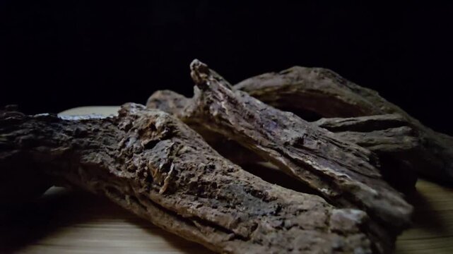 Macro shot of raw Indian Costus roots (Saussurea costus) on a wooden surface. High-quality footage showcasing the natural, dried woody texture of this ancient medicinal herb.