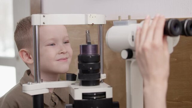 Doctor ophthalmologist and Young boy looking into slit lamp during eye exam clinic.
