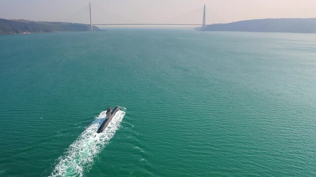 Turkish navy submarine underway in Bosphorus Strait heading toward Yavuz Sultan Selim Bridge in wide aerial shot with seagull and turquoise water