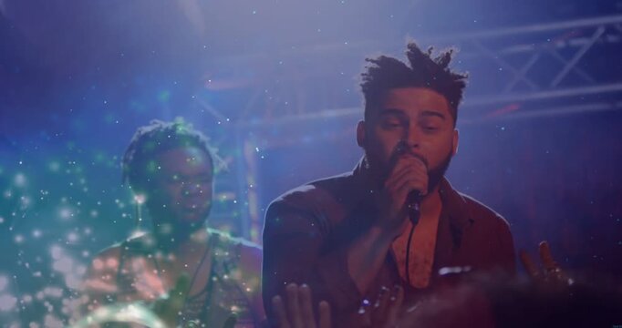 Lead singer bringing mic to mouth singing and engaging music crowd sparkles drifting near singer