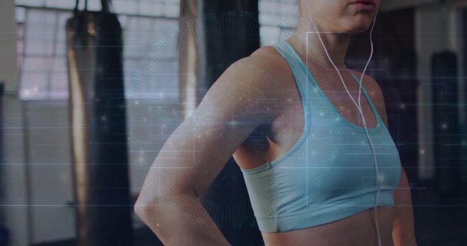 Vertical video: Showing woman in blue bra fixing wired earbuds while camera pulling in gym resting