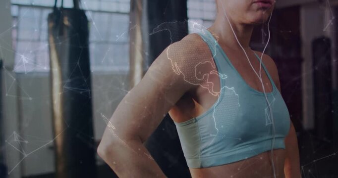 Vertical video: Overlay appearing, woman in bra with wired earbuds prepping near heavy bags in gym