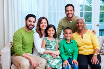 Portrait of multiethnic family smiling at camera while sitting together at home, showing bonding across generations. Ideal for family insurance, parenting, healthcare, community support marketing