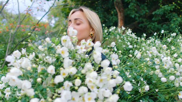 Beautiful Caucasian woman holding a huge bunch of white flowers. Blonde lady among the flowers outdoors.