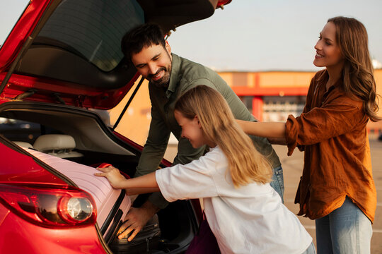 Family with child girl preparing for road trip, loading their car with luggage and chatting