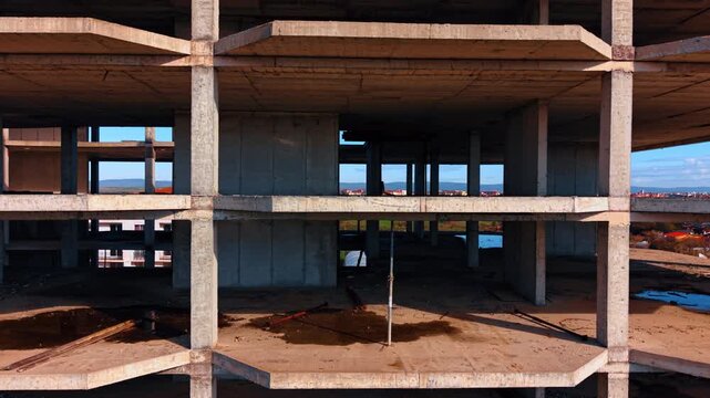 Front view of multi story unfinished concrete building frame. Symmetrical exterior view of a concrete skeletal structure under construction with a landscape background.