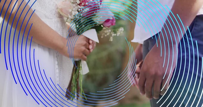Vertical video: Reaching man joining hands with woman in white on bouquet in garden blue rings