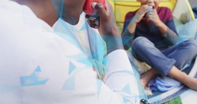 Camera pulling back showing man in white shirt lifting apple, sharing snack beside boy in tent