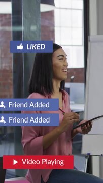 Vertical video: Woman checking tablet in office causing social alerts, laughing then refocusing