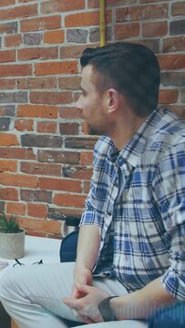 Vertical video: Man sitting in office responding to left speaker, turning, smiling, watching phone