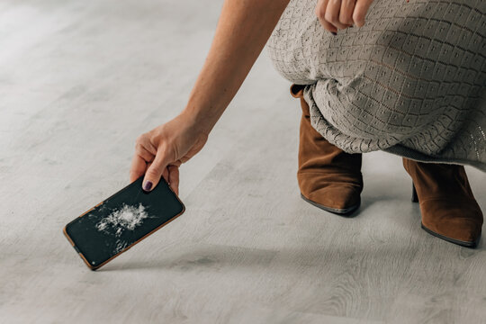 woman picking up a broken mobile phone from the floor after a fall or accident