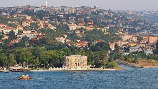 K&uuml;&ccedil;&uuml;ksu Pavilion Ottoman Baroque palace on Bosphorus waterfront with small boat passing and hillside residential neighborhood, Istanbul