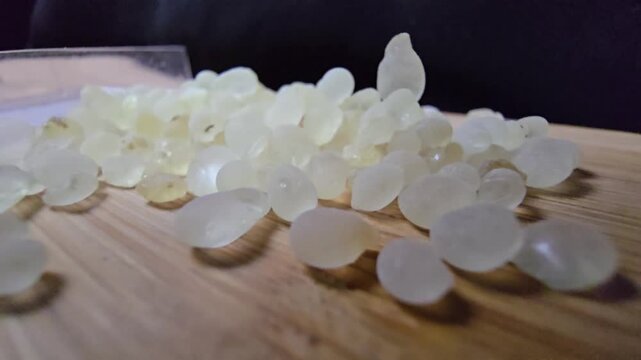 Macro shot of premium Mastic gum (Pistacia lentiscus) tears on a wooden surface. High-quality footage showcasing the translucent, pale yellow resin used in medicine and cooking.