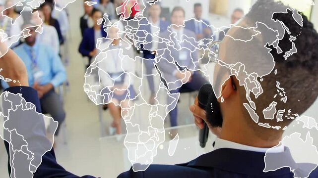 Presenter raising hand and speaking into mic, initiating world map overlay across business audience