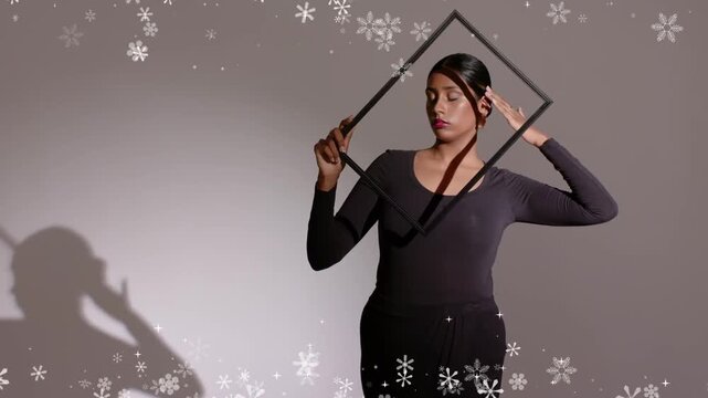 Woman model holding square frame, posing and tilting, casting shadow with snow overlay for fashion