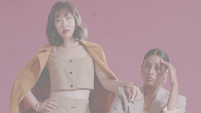 Vertical video: Second model entering left, draping coat and touching seated model, posing fashion